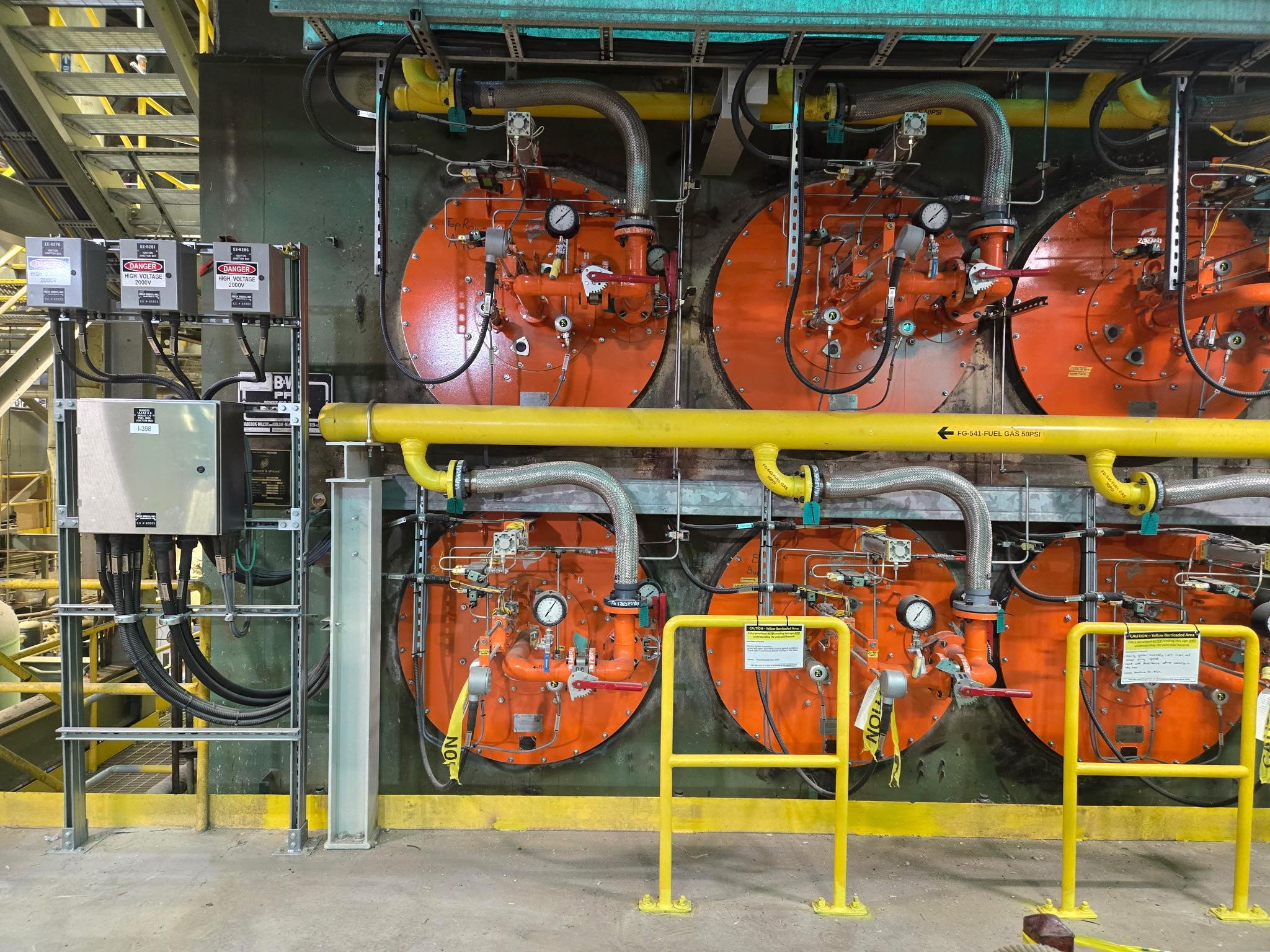 Boiler burner fronts with fuel gas piping and high-voltage junction boxes at Mosaic Belle Plaine.